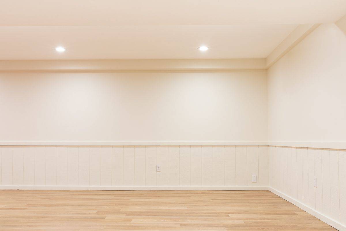 An empty basement with white walls and a medium toned vinyl plank flooring.