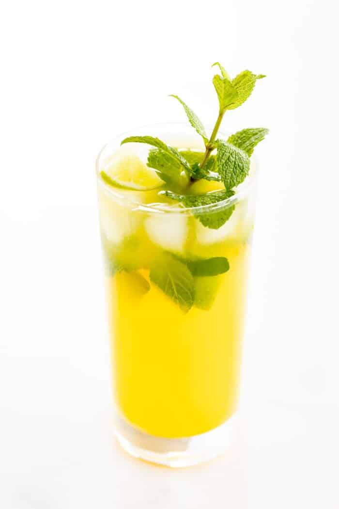 A mango mojito in a clear glass, garnished with a sprig of mint.