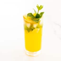 A mango mojito in a clear glass, garnished with a sprig of mint.