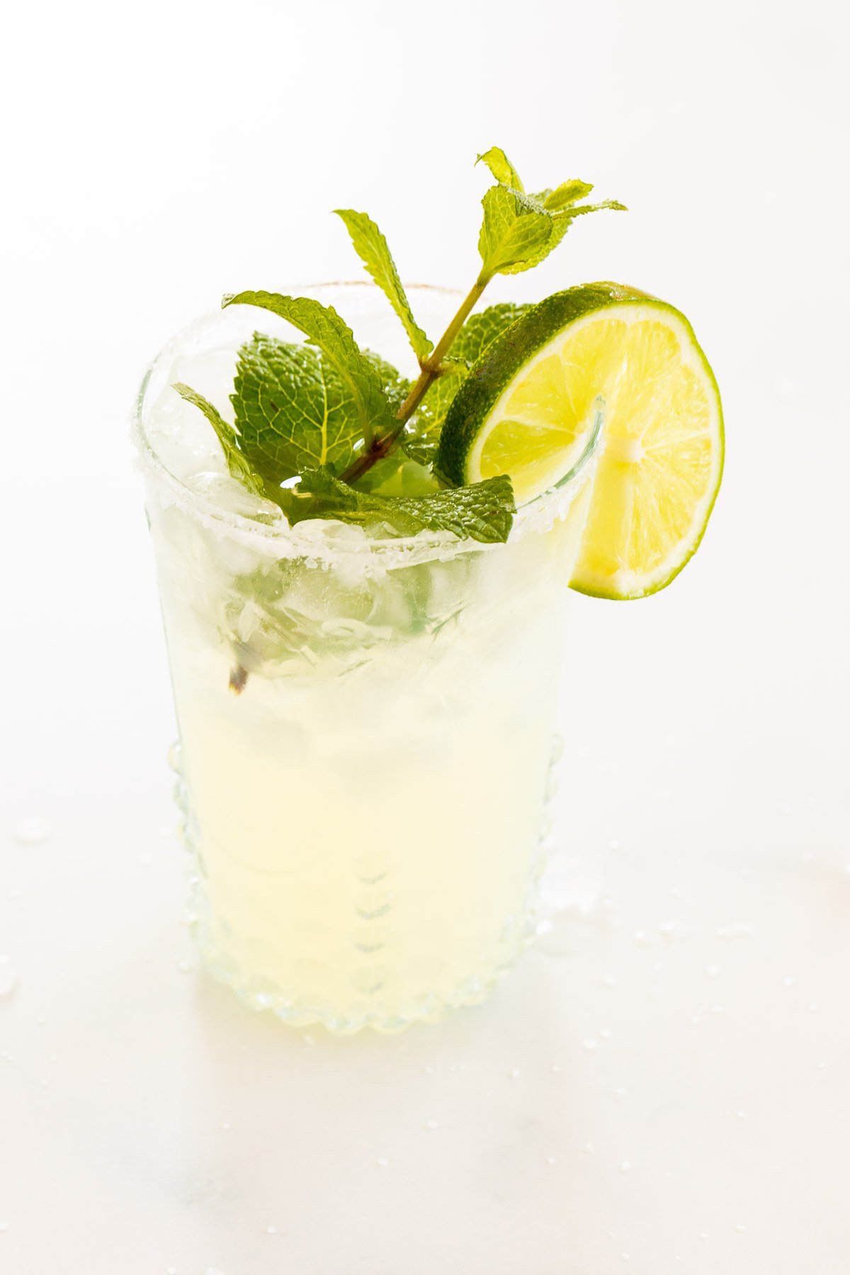 A mint margarita in a clear glass on a white surface