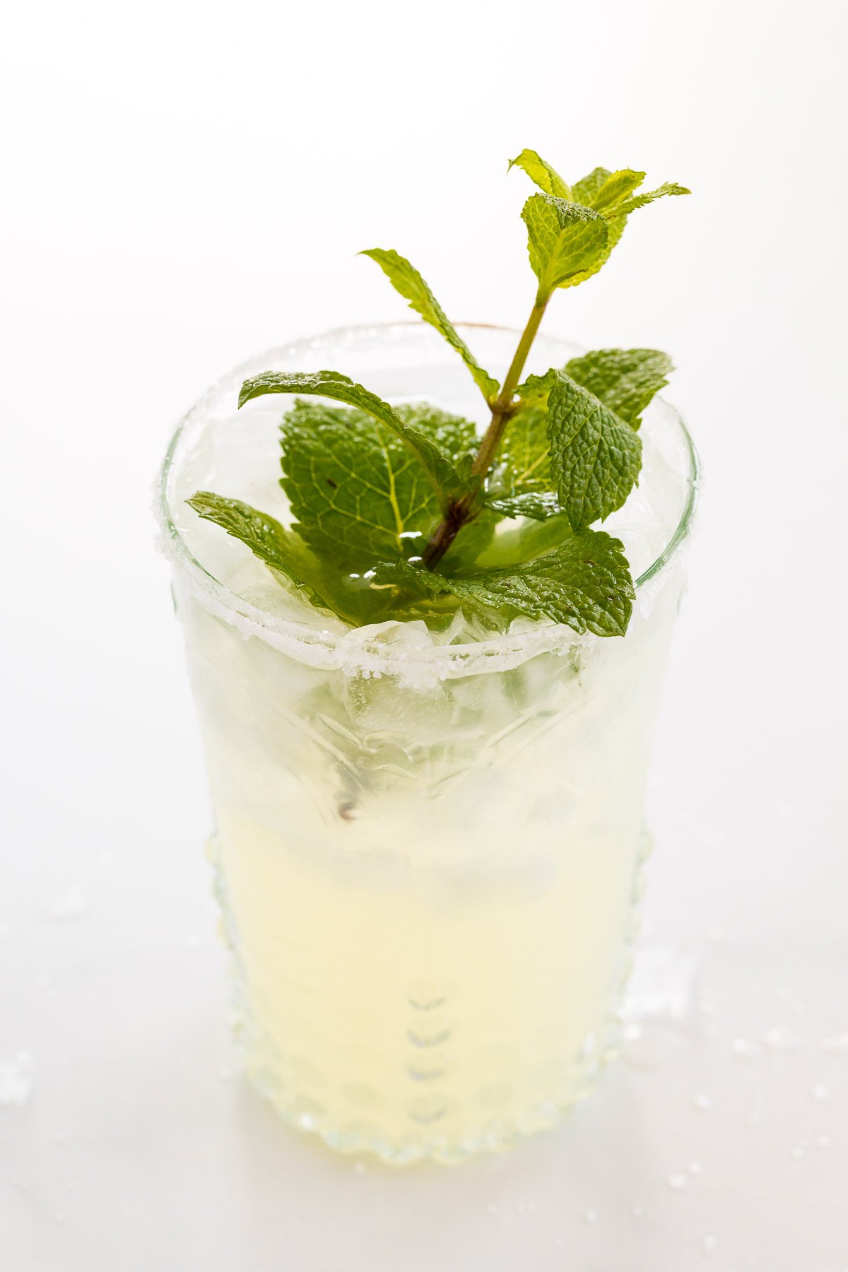 A mint margarita in a clear glass on a white surface