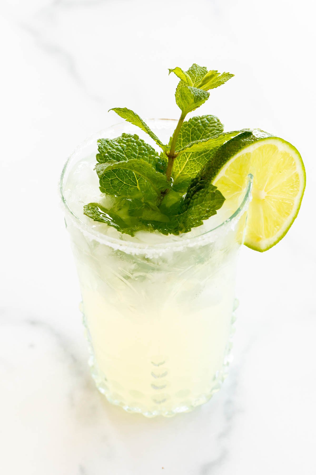 A mint margarita in a clear glass on a white surface