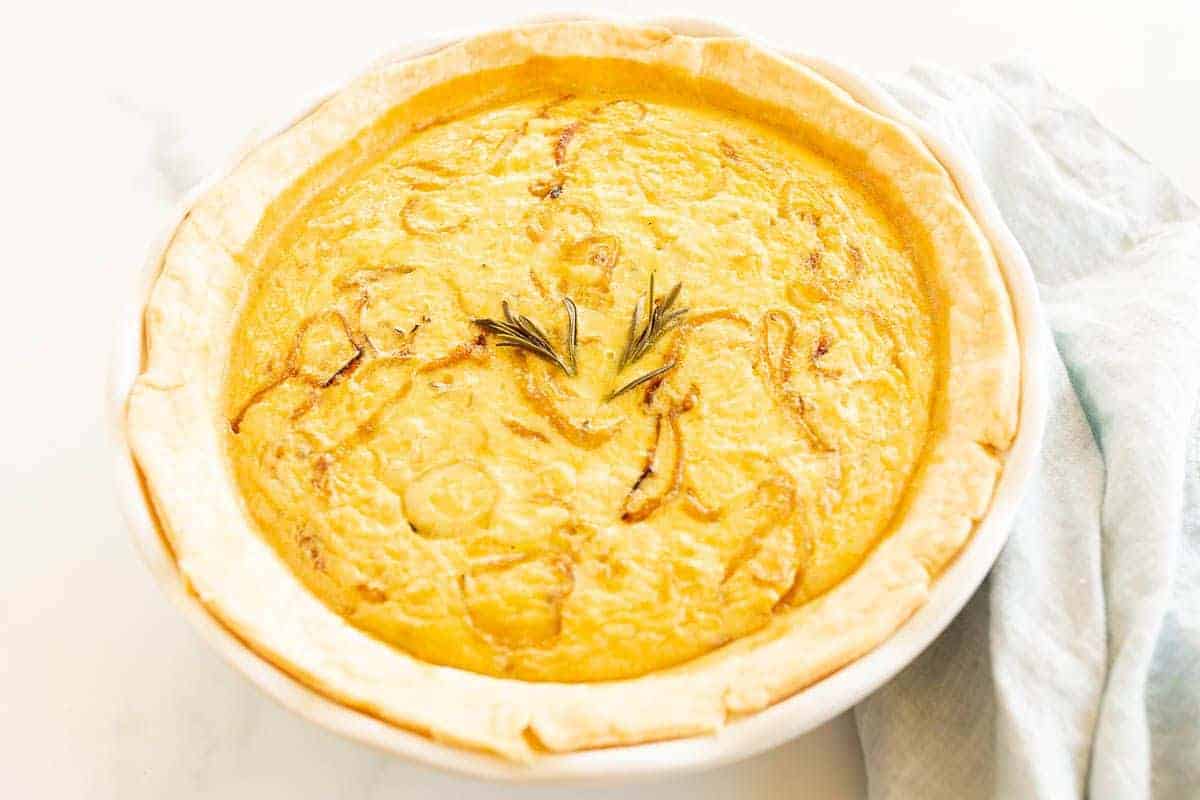 A caramelized onion quiche baked in a white pie pan on a marble surface.