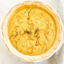 A caramelized onion quiche baked in a white pie pan on a marble surface.