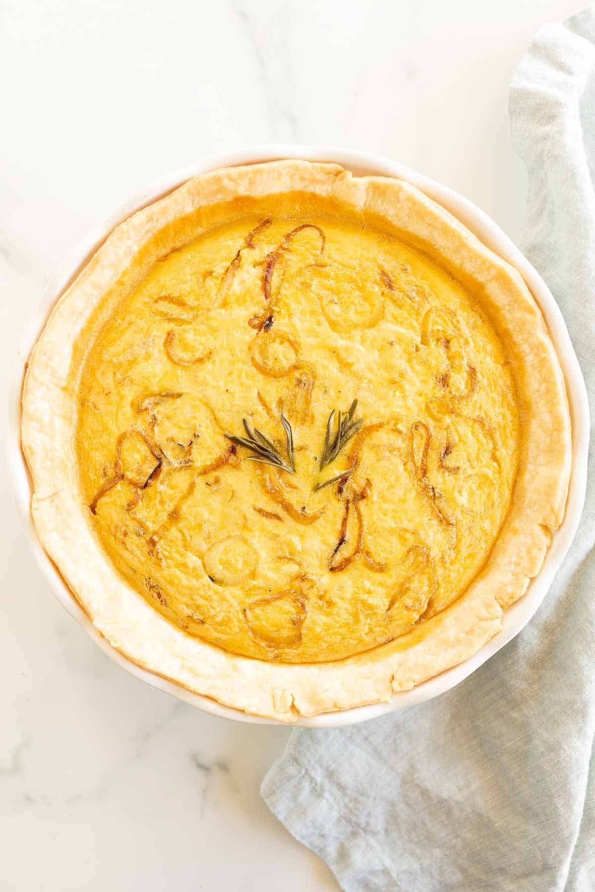 An onion quiche baked in a white pie pan on a marble surface.