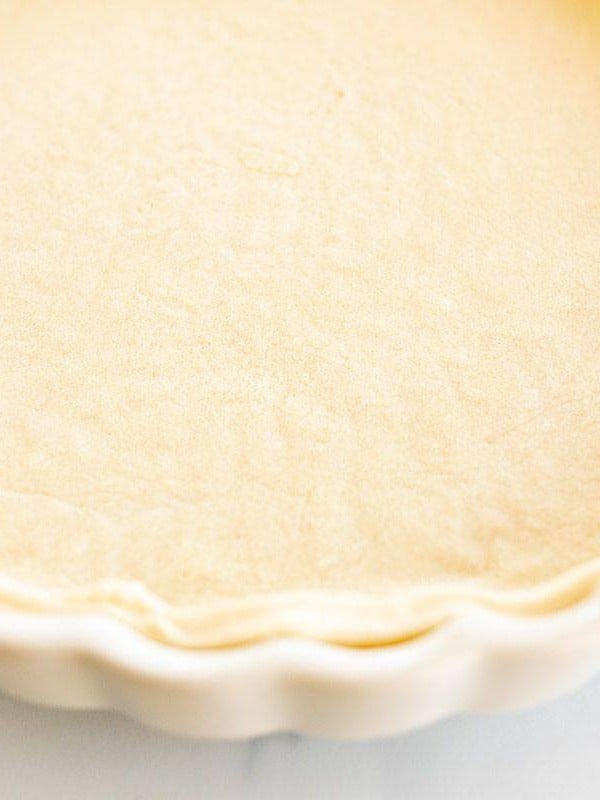 A homemade quiche crust in a fluted pie pan on a white marble surface.