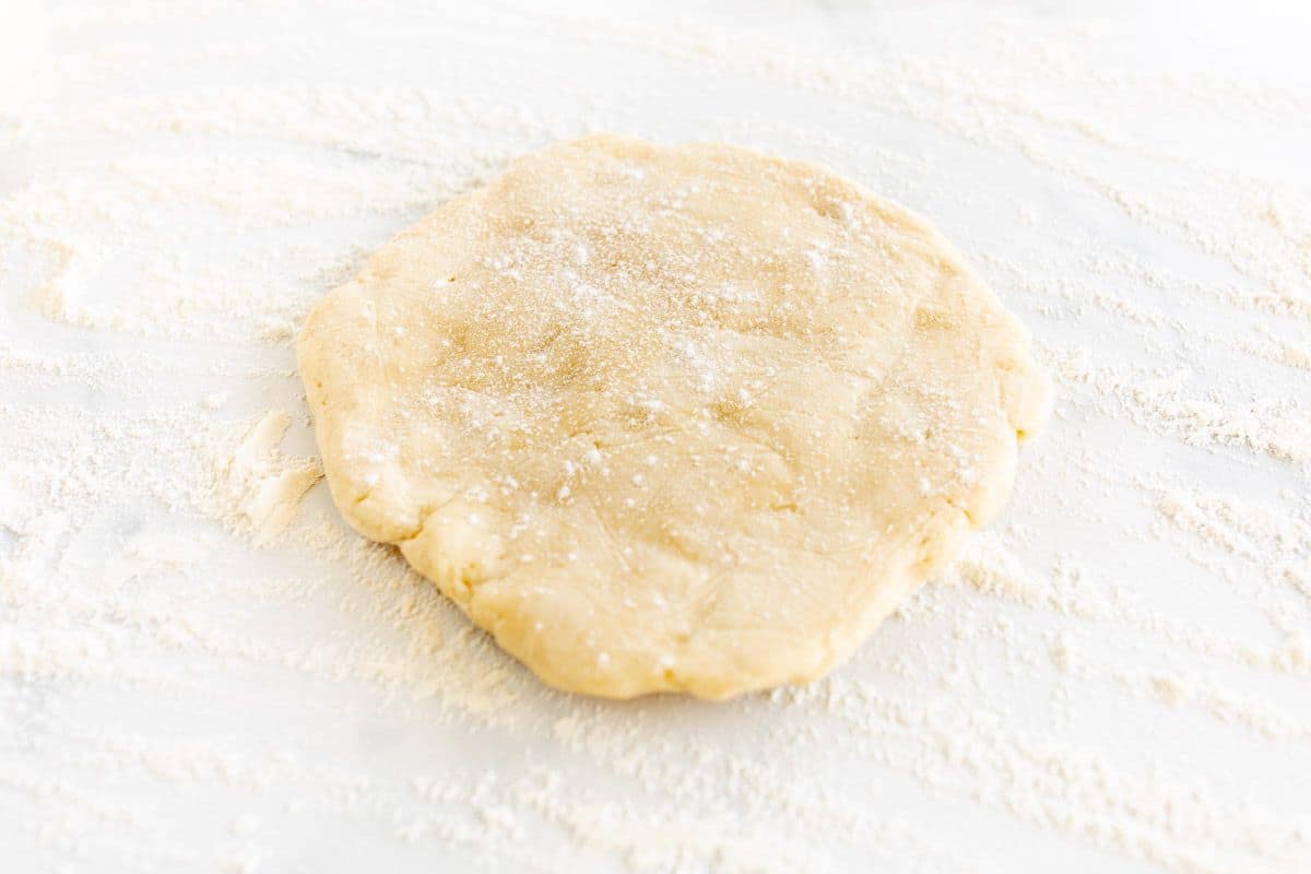 A quiche crust on a marble surface, dusting of flour underneath.