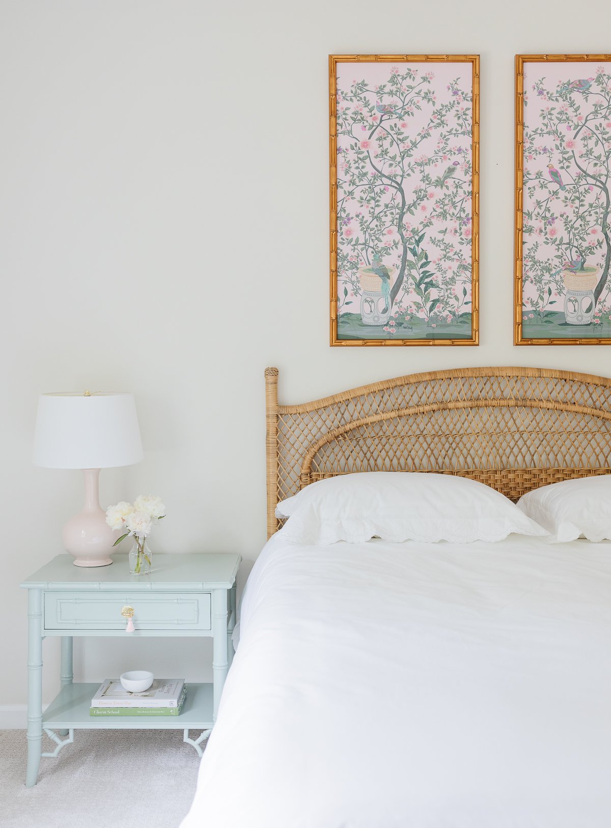 A bedroom with a rattan bed and two paintings on the wall.