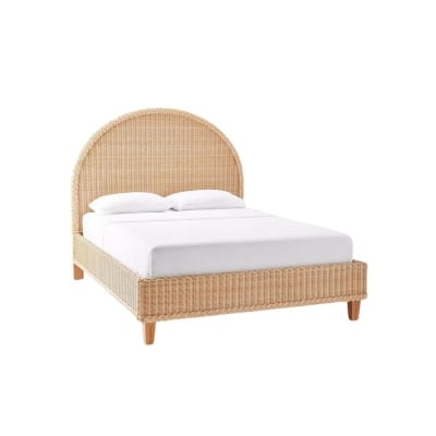 A rattan bed with white sheets and wooden legs.