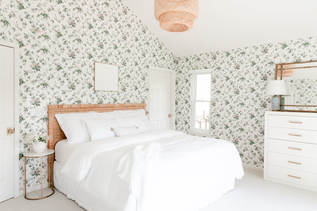 A bedroom with floral wallpaper, a white dresser, and a rattan bed.