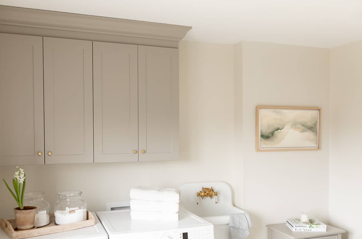 A laundry room with gray cabinets, Samsung The Frame TV, and a small white sink.