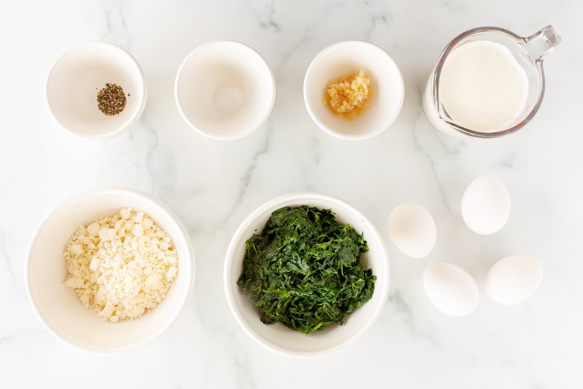 ingredients for spinach and feta quiche laid out on a marble countertop.