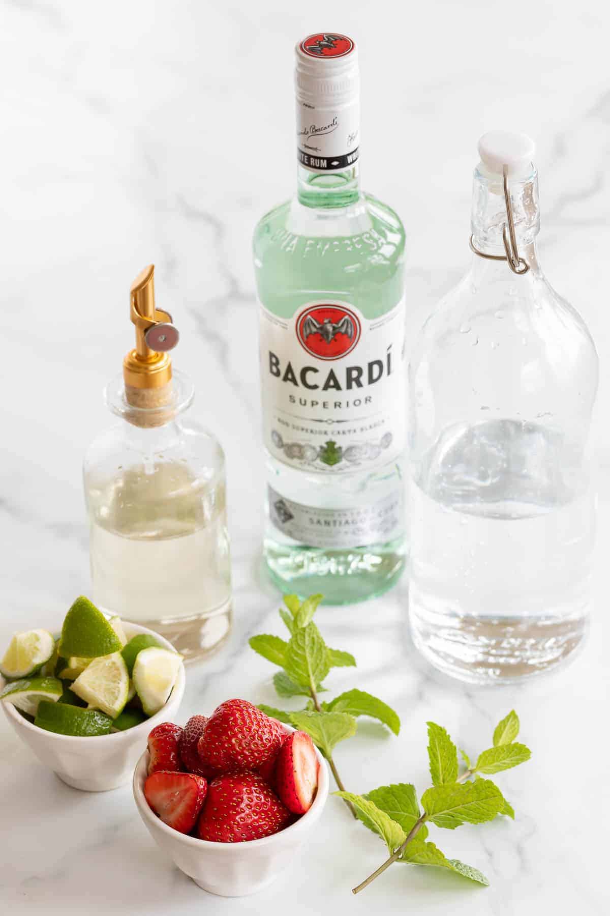 rum simple syrup club soda strawberries limes and mint on marble counter