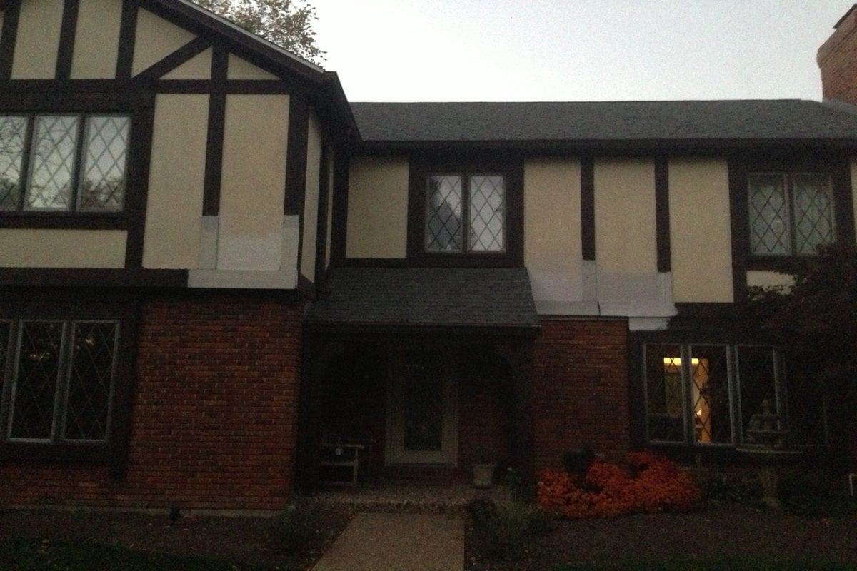 A dark vintage tudor home, with brick on the bottom and light yellow and brown trim up top.