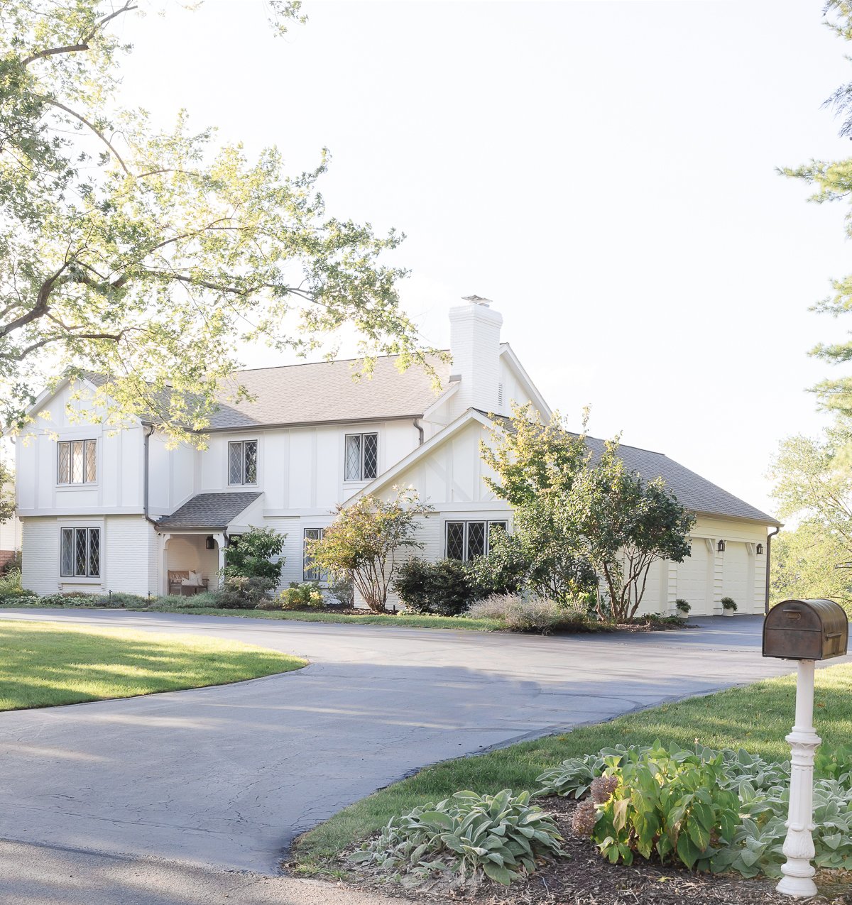 A spacious two-story house with a Benjamin Moore Swiss Coffee exterior, manicured lawn, and driveway, captured on a sunny day.