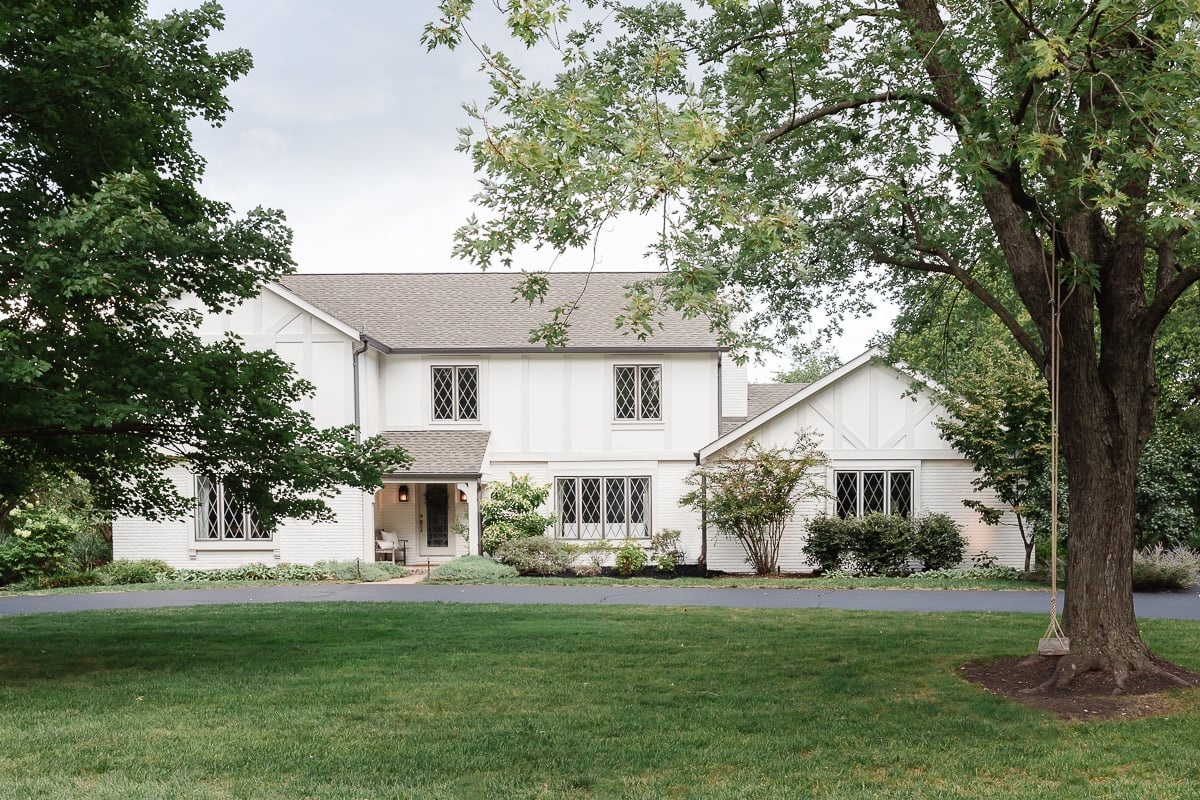 A large, white two-story house painted in Benjamin Moore Swiss Coffee, with a gabled roof, surrounded by green lawn and trees.