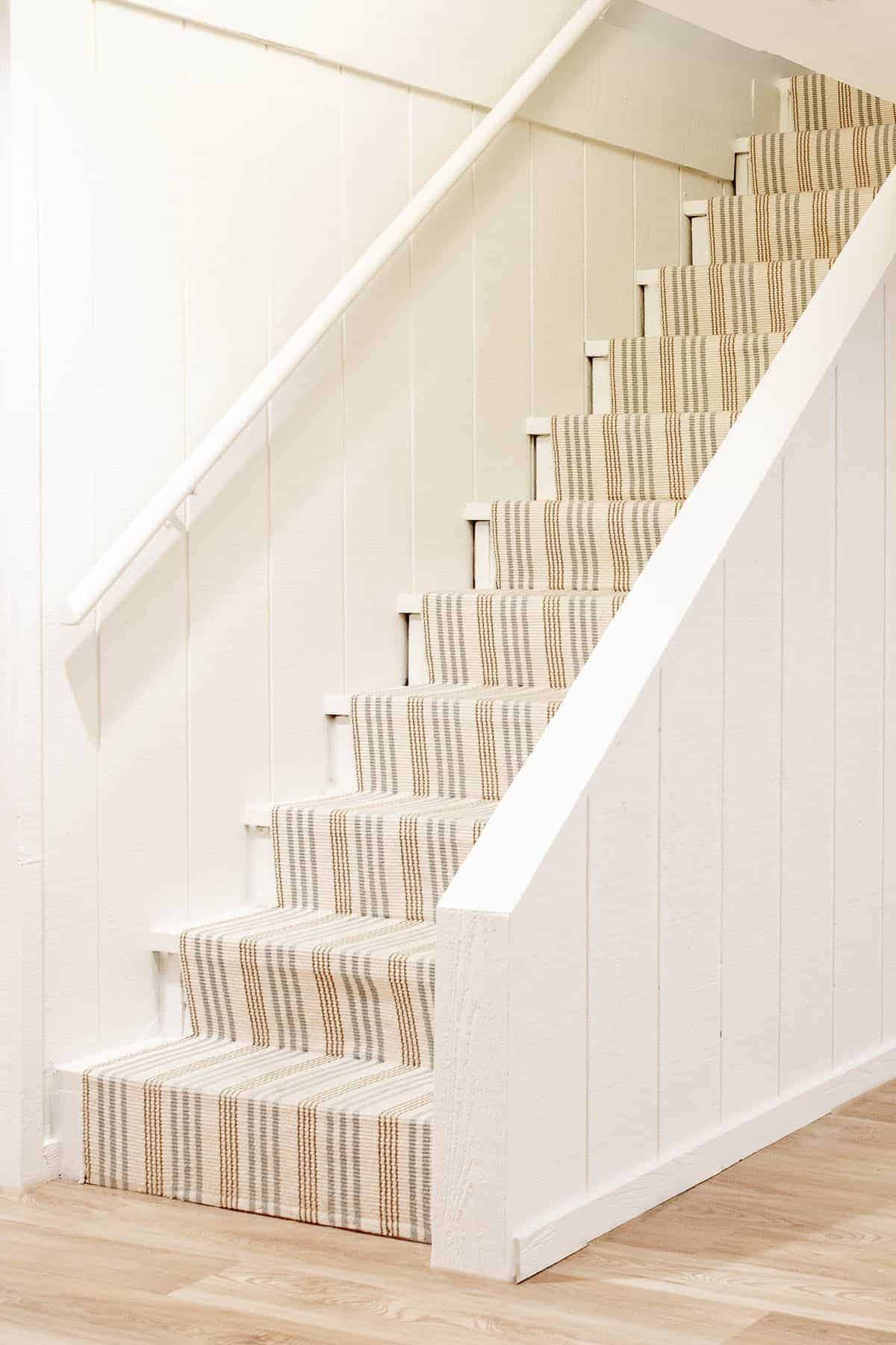 Basement stairs with a striped runner and Benjamin Moore Swiss Coffee neutral paint color on the walls.