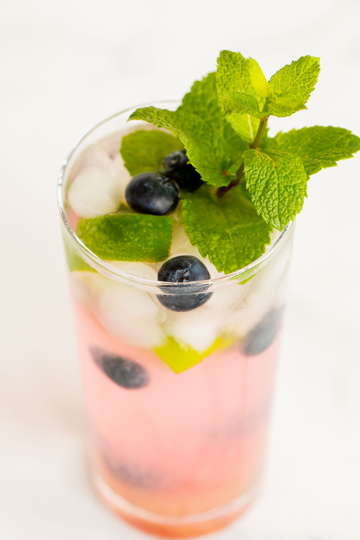 A fresh blueberry mojito garnished with mint, lime and blueberries on a marble surface.