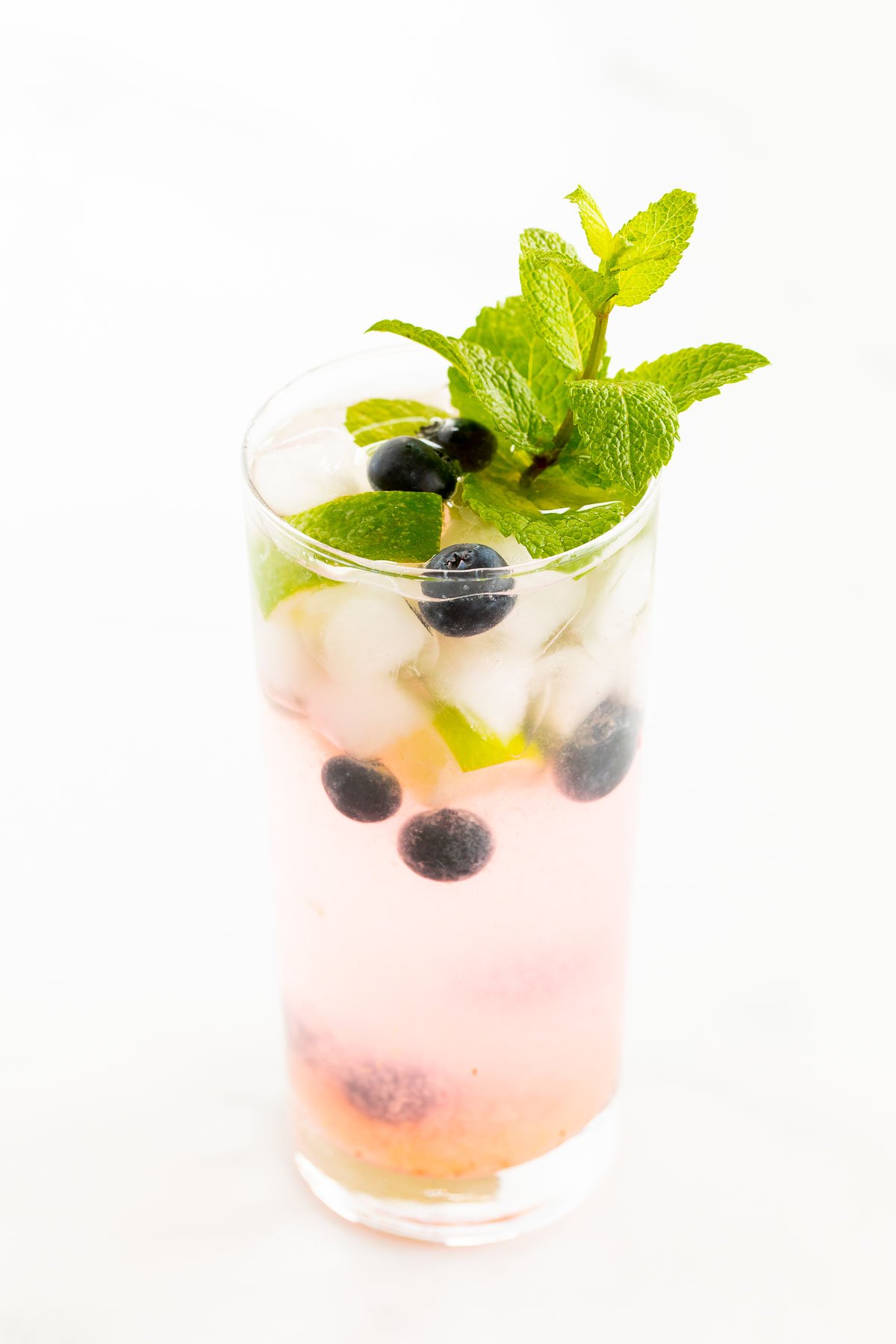 A fresh blueberry mojito garnished with mint, lime and blueberries on a marble surface.