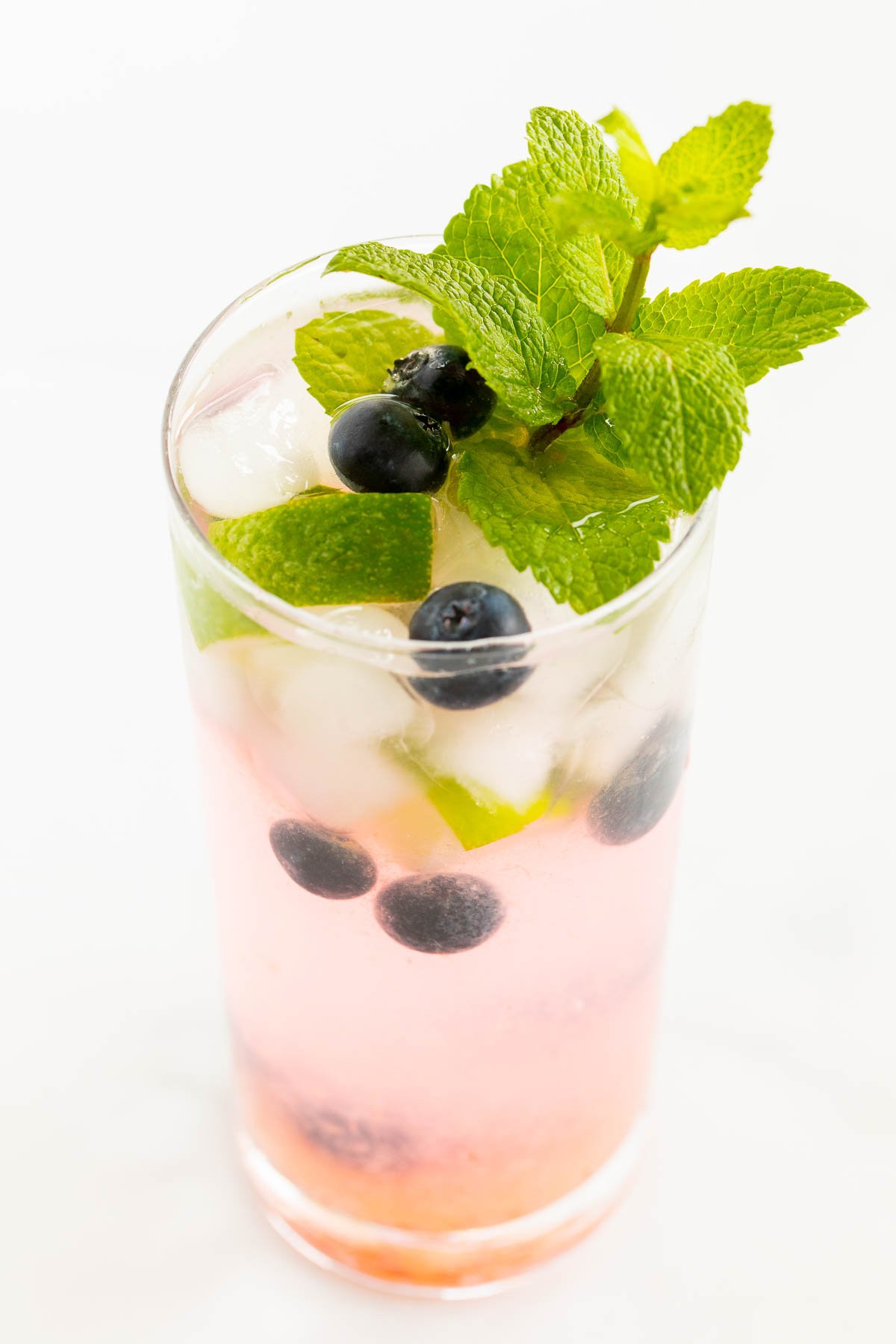 A fresh blueberry mojito garnished with mint, lime and blueberries on a marble surface.