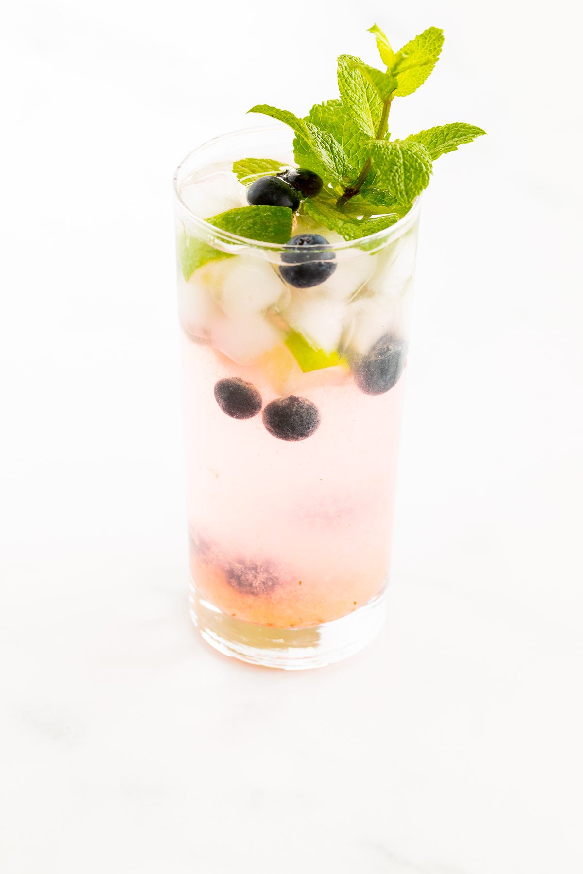 A fresh blueberry mojito garnished with mint, lime and blueberries on a marble surface.