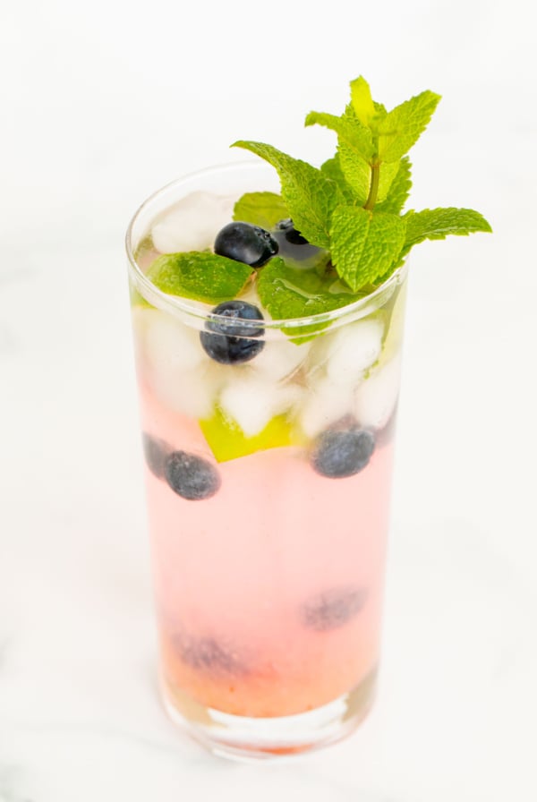 A fresh blueberry mojito garnished with mint, lime and blueberries on a marble surface.