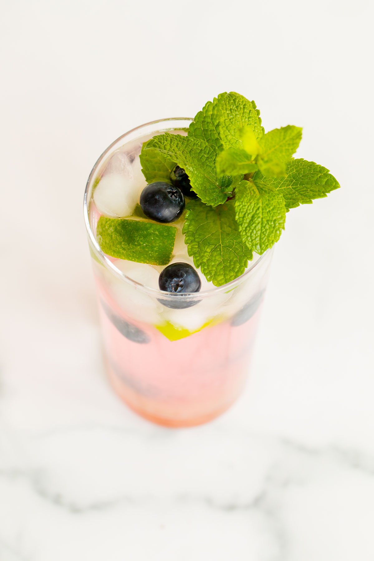 A fresh blueberry mojito garnished with mint, lime and blueberries on a marble surface.