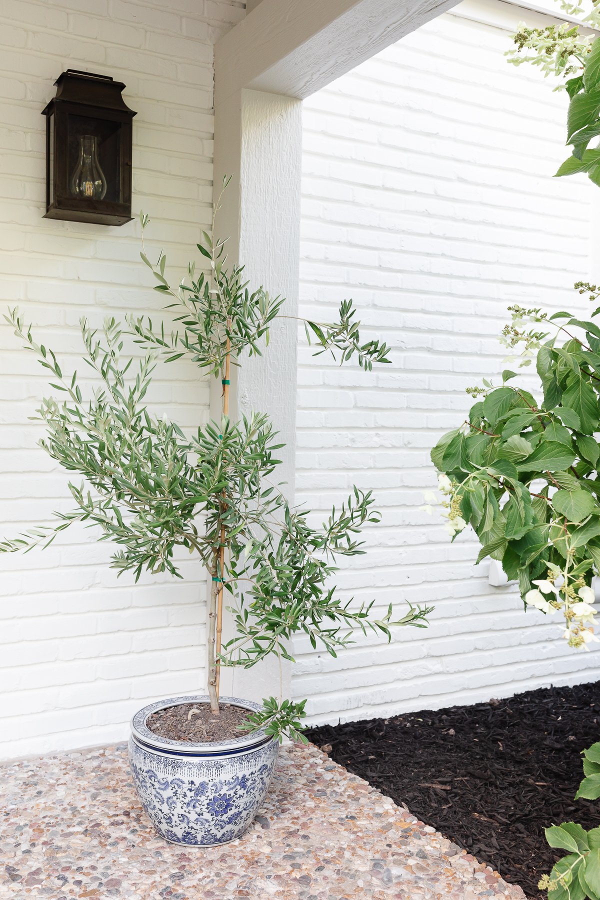 An entryway to a white brick home with copper lanterns on either side of the wooden Dutch door.