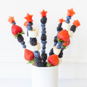 Red white and blue fruit skewers with a star on top in a white jar for display.