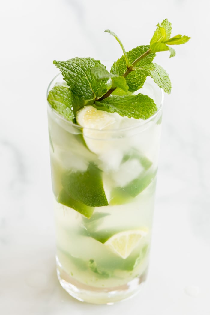 A clear glass full of a gin mojito on a marble countertop.