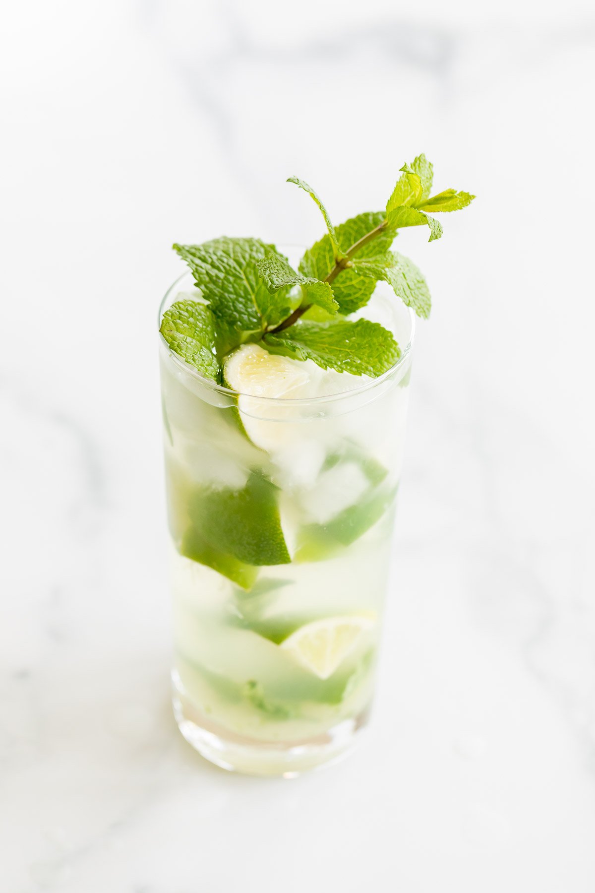 A clear glass full of a gin mojito on a marble countertop.