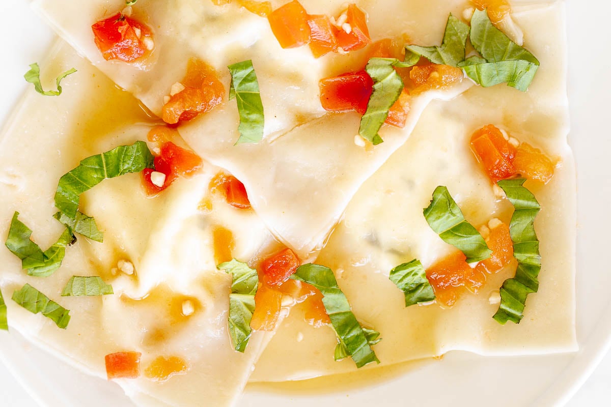 Homemade goat cheese ravioli with basil on a white plate with a gold fork.