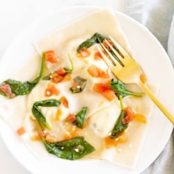 Homemade goat cheese ravioli with basil on a white plate with a gold fork.