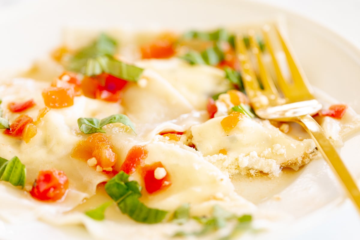 Homemade goat cheese ravioli with basil on a white plate with a gold fork.