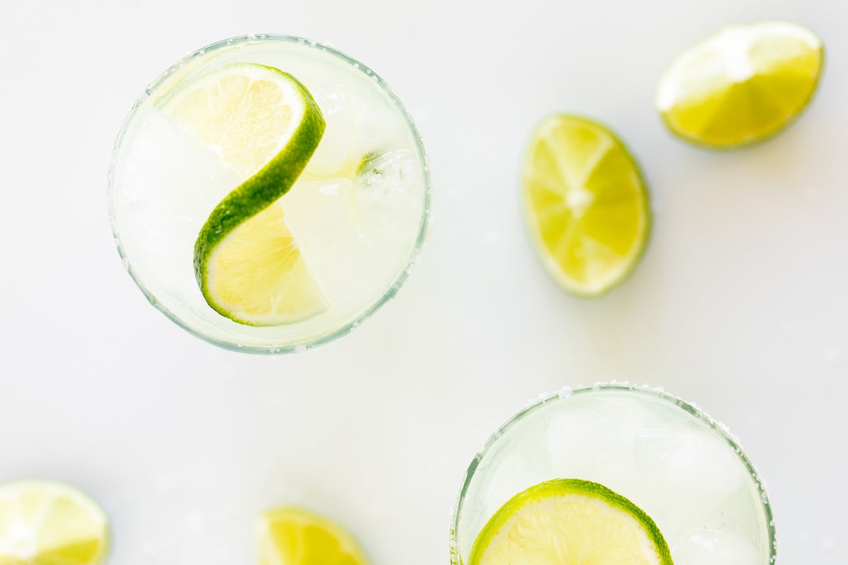 A homemade margarita recipe served up in clear glasses with limes