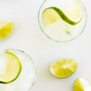 A homemade margarita recipe served up in clear glasses with limes