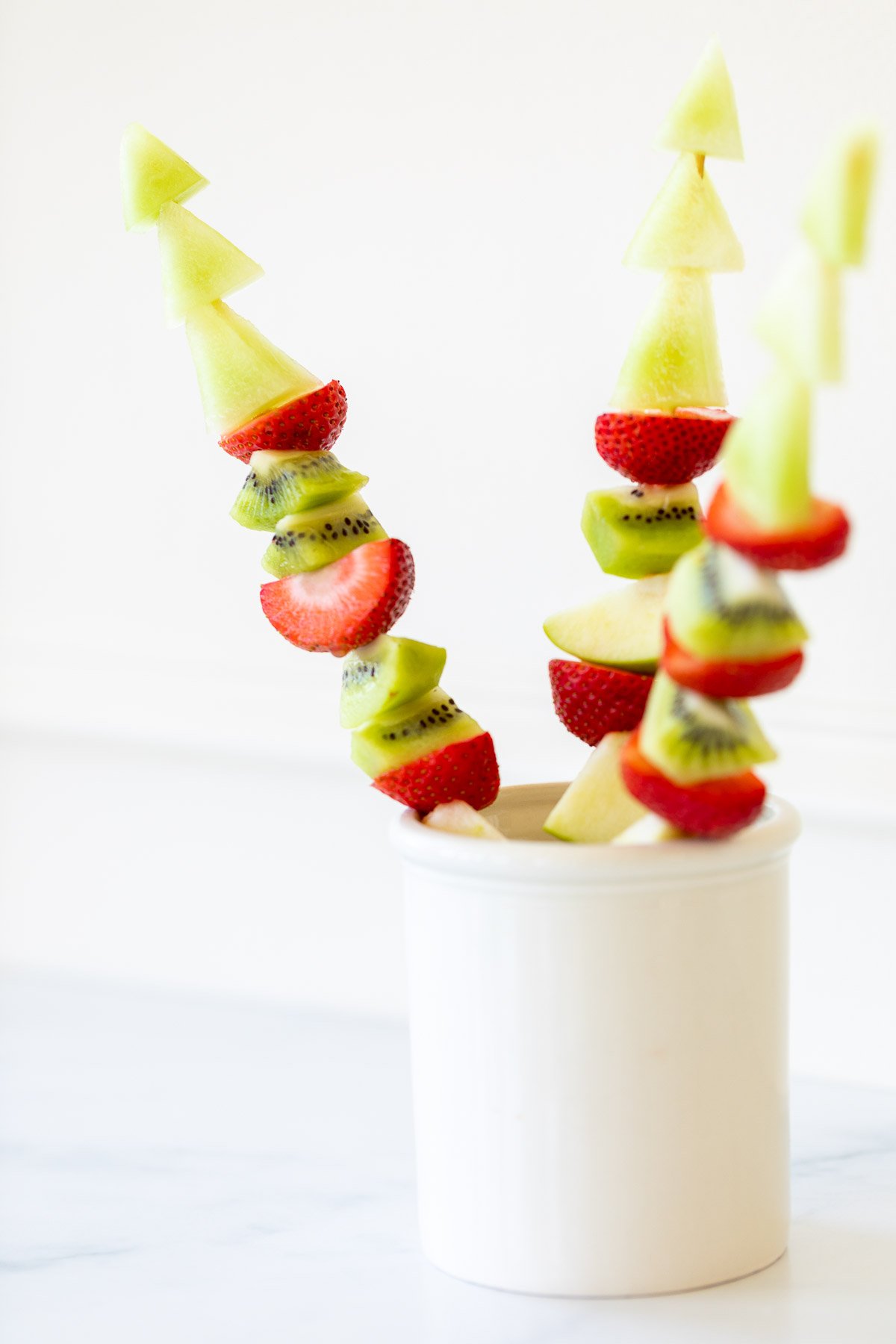 Green and red fruit skewers in a white container.