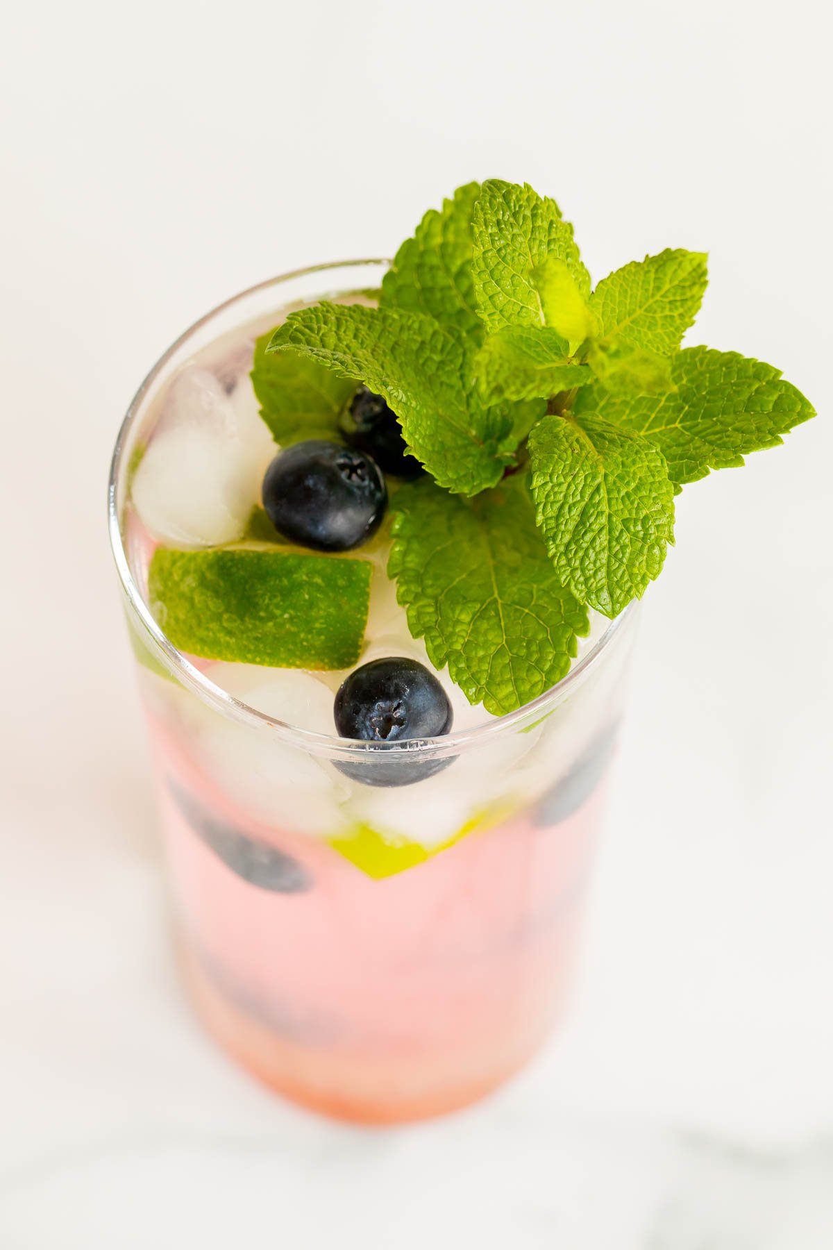 A fresh blueberry mojito garnished with mint, lime and blueberries on a marble surface.