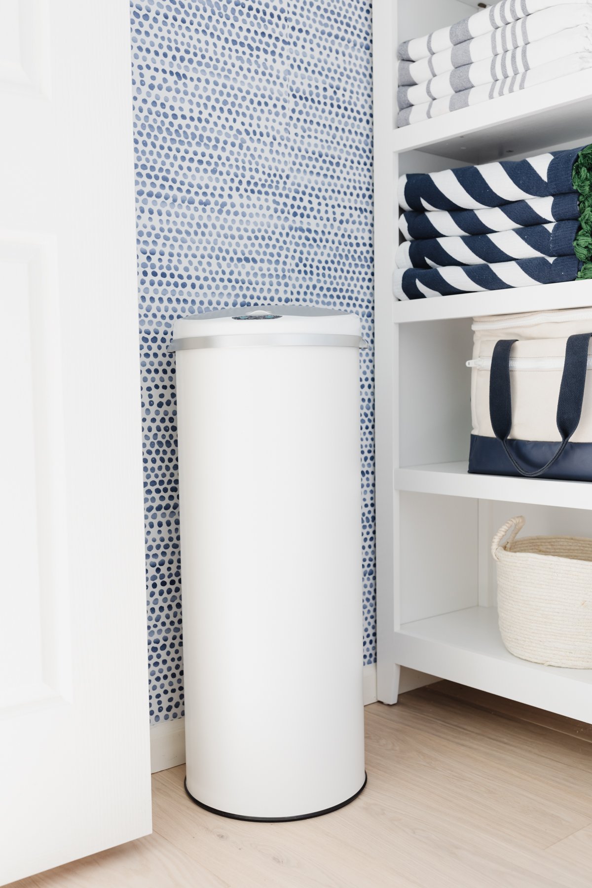 A white trash can in a laundry closet.