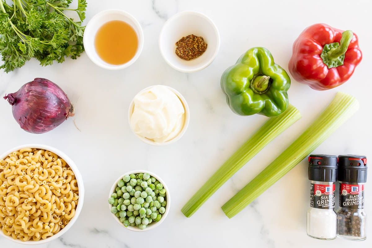 Fresh ingredients for macaroni salad laid out on a marble countertop.