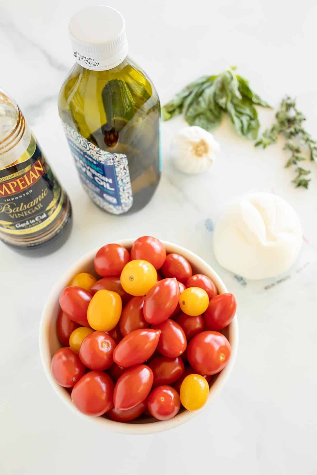 Ingredients for a baked burrata recipe, including cherry tomatoes, olive oil, burrata cheese and more.