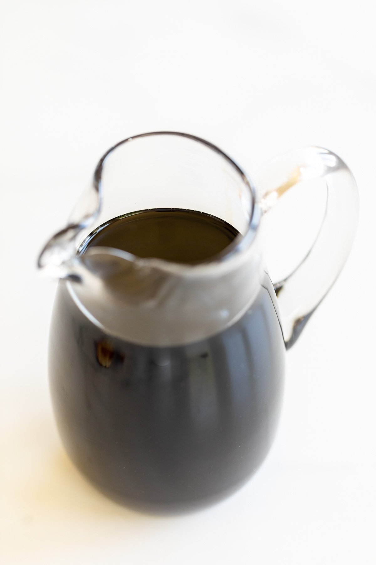 A clear glass pitcher full of balsamic glaze on a marble countertop.