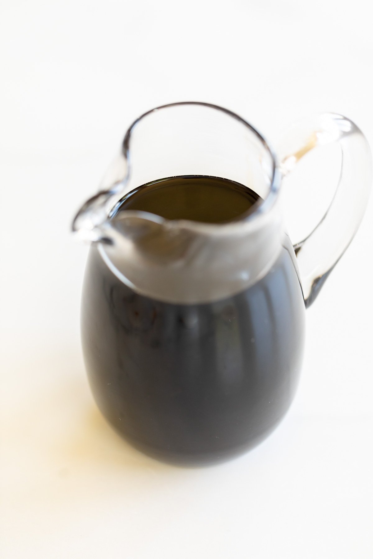 A clear glass pitcher full of balsamic glaze on a marble countertop. 