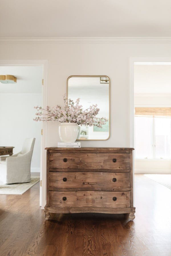 An entryway with a wooden chest and pink flowers in a vase