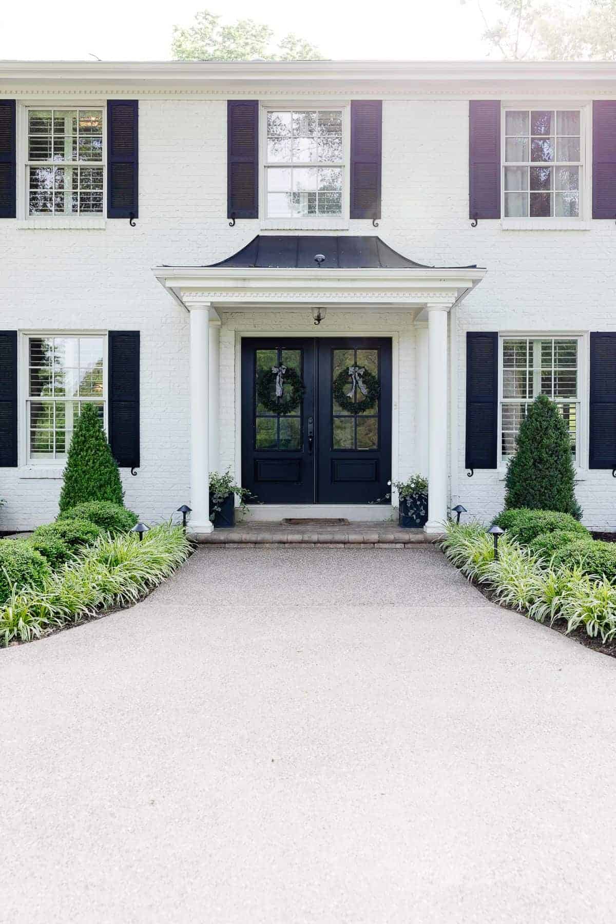 A colonial brick house painted in Benjamin Moore Simply White with black shutters.