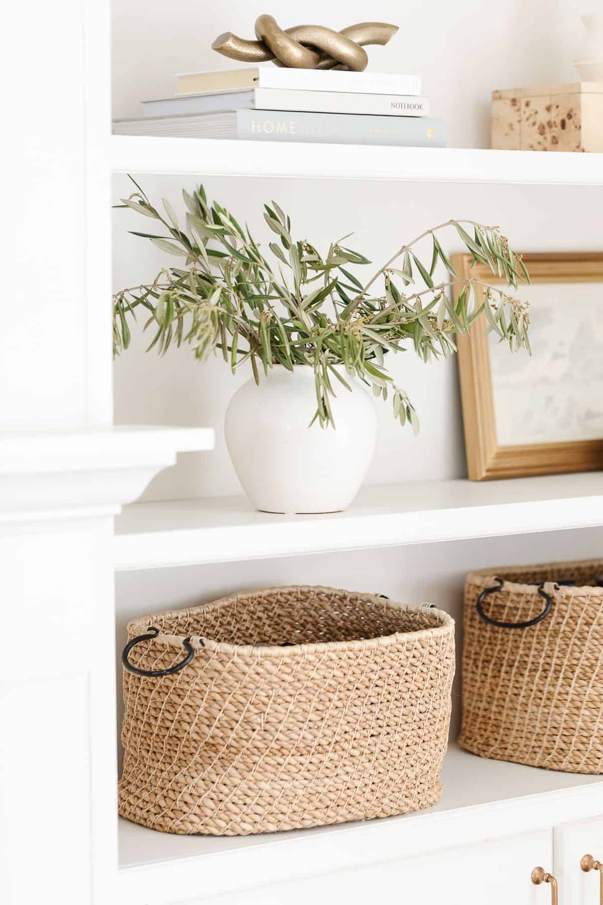 Bookshelf decor ideas of baskets, white pottery and artwork on white built ins.