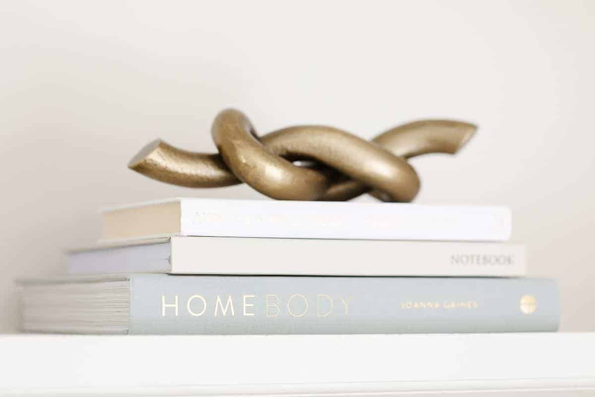 White books with a gold metal decorative knot accent on top for bookshelf styling.