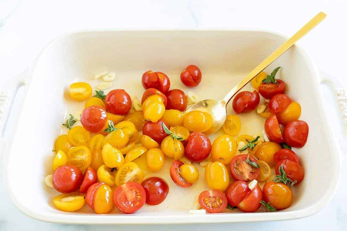 Diced cherry tomatoes in a white baking pan, gold spoon to the side.