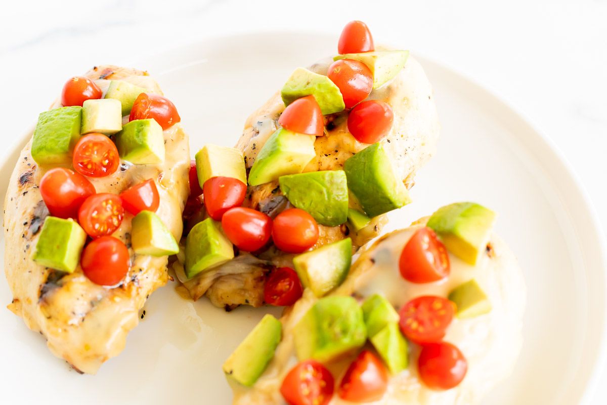 California chicken grill on a white plate, topped with diced avocado and tomato.