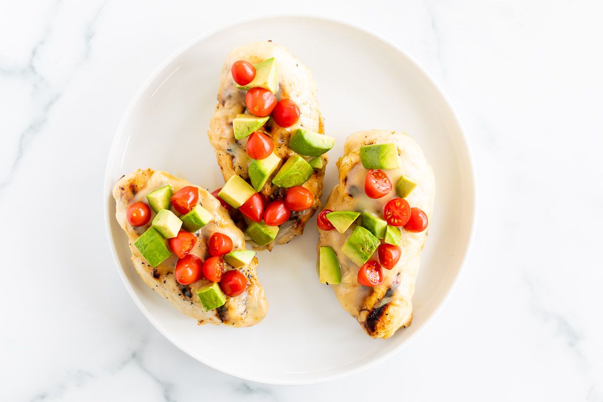 California chicken grill on a white plate, topped with diced avocado and tomato.